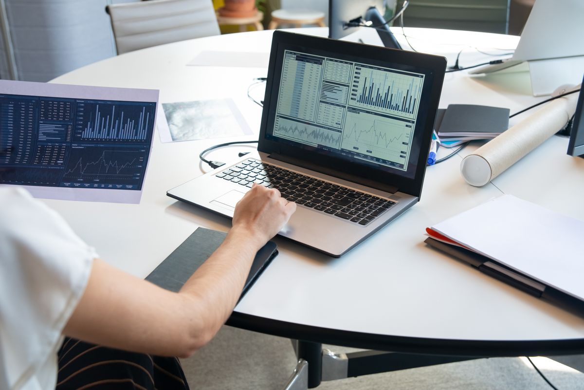 Pessoa analisando gráficos em um notebook e em relatórios impressos